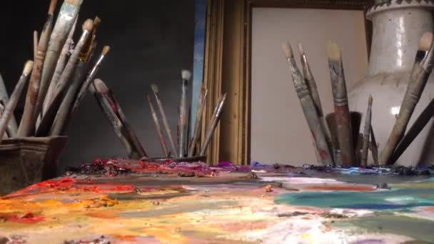 Oil paintings in creative workroom. Brushes, paints, palette, canvas, easel — 图库视频影像