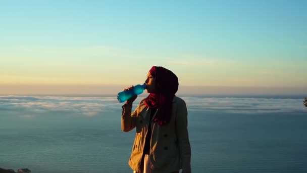 Wiederverwendbare Glas-Wasserflasche vorhanden. Null Verschwendung ohne Plastik. Muslimische Frau trinkt Wasser mit Ökoflasche. Meeresküste — Stockvideo