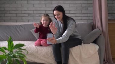 Gülümseyen anne ve çocuk, babalarıyla görüntülü konuşma yaparken el sallıyor ve kalplerini gösteriyorlar. Ellerin, kalbin ve sevginin jesti