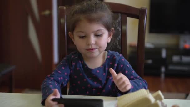 Mała dziewczynka używa smartfona w domu sama. Gry online, sieci społecznościowe, Internet — Wideo stockowe