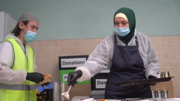 Ramadan Support Vrijwilliger. Islamitische hulp en hulp. Moslimvrijwilligers met een hijab, masker en handschoenen. Koken van voedsel, verpakking van warme maaltijden in lunchdozen voor behoeftigen — Stockvideo