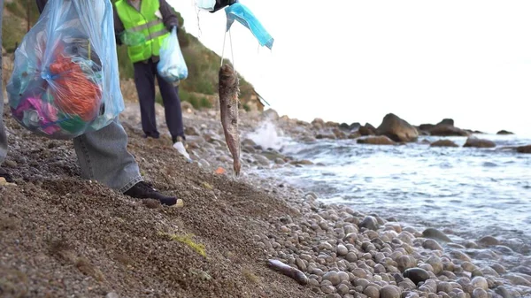 Los peces marinos se enredan en las correas de las orejas de las máscaras faciales y mueren. Máscaras y guantes desechados en la playa del océano. Eliminado incorrectamente, el PPE mata la vida marina. Voluntarios recogen basura en la playa — Foto de Stock