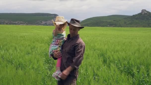 Ein Bauernvater mit einer glücklichen kleinen Tochter im Arm inspiziert ein Weizenfeld. Biologischer Familienbetrieb. Das Leben im Dorf. Erntekonzept für die Landwirtschaft — Stockvideo