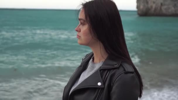 Retrato de uma jovem e triste mulher morena moderna, em uma jaqueta de couro andando na costa do mar de inverno — Vídeo de Stock