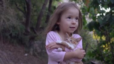 Sevimli bebek arka bahçede küçük kırmızı bir kedi yavrusuna sarılıyor.