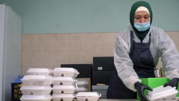 Ід аль-Адха або Свято Жертвопринесення. Ісламська допомога та допомога. Мусульманська жінка-волонтер у хіджабі, масці та рукавицях. Готувати їжу, пакувати гарячі страви в коробках для обіду, роздавати нужденним. — стокове відео