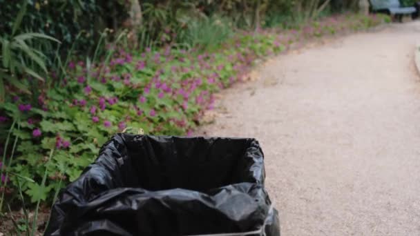 Uma mulher joga uma máscara médica descartável usada em uma lata de lixo. Lá fora, no parque. COVID-19 - pandemia e poluição ambiental — Vídeo de Stock