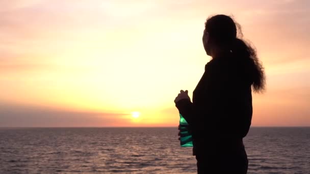 Viaggio libero di plastica. Una viaggiatrice sull'oceano al tramonto beve acqua da una bottiglia riutilizzabile — Video Stock