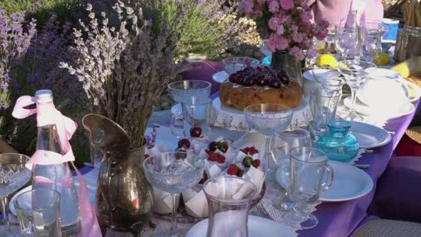 Romantisk sommarpicknick på lavendelfältet. På bordet finns muffins, frukt, glas vin, och en bukett blommor — Stockvideo