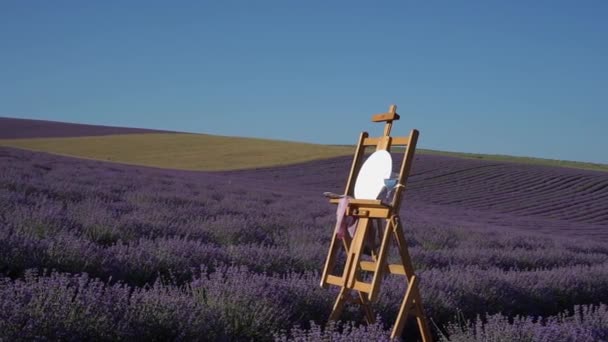 Egy festőállvány kerek vászon festék- és ecsetpalettával. Kellemes levegő a természetben. Kilátás a levendula és a búza mező. Tájkép Provence-ban Franciaország — Stock videók