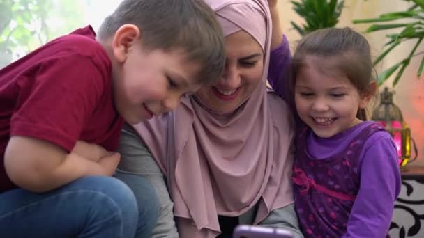 Happy Eid al-Adha Celebrations Online. Happy traditional Muslim family, mother in hijab and children together at home using smartphone to call friends during lockdown. Eid mubarak — Stok video