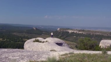 Yetişkin bir kadın uçurumun kenarında duruyor ve elleri havada gökyüzüne bakıyor.