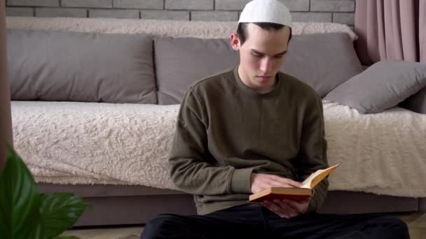 Мусульманський студент читає книжку вдома, сидячи на підлозі. Традиційна школа релігійної освіти, дистанційне навчання, блокування. Підліток - юнак вчиться. — стокове відео