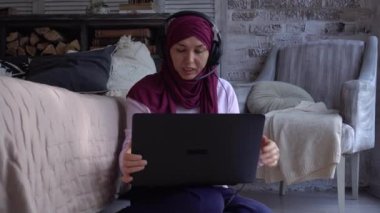 Mutlu gülümseyen Müslüman kadın uzaktan çalışıyor. Kilitlenme, çevrimiçi sohbet, iş konferansı kulaklık, mikrofon ve dizüstü bilgisayar. Uzaktan çalışma, serbest çalışma, eğitim. Uzaklık öğrenme öğretmeni