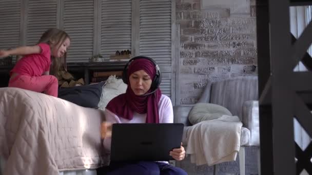 Moderne Multitasking muslimische Mutter arbeitet entfernt ist gestresst. Frauen arbeiten mit Baby von zu Hause aus. Lautes aktives Mädchen beim Spielen. Online-Chat, Geschäftskonferenz über Kopfhörer. Flexibler Job — Stockvideo