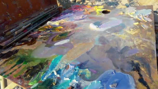El artista mezcla pinturas al óleo en la paleta con un pincel. Terapia artística. Pintura al aire libre, naturaleza, paisaje — Vídeo de stock