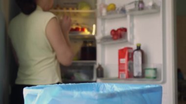 Çöpe yemek atıkları atmak. Ev yemeği kaybı. Uygun olmayan depolama nedeniyle evdeki yiyecek bozulması meydana gelir. Bir kadın yenmemiş yiyecekleri buzdolabından dışarı atar.