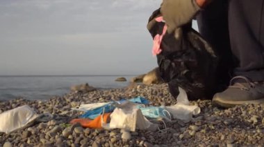 Covid-19 ve dünya okyanuslarının kirliliği. Coronavirus plastik atığı, kullanılmış yüz maskesi, okyanusta eldivenler. Çöp toplayıcısı ya da gönüllü, deniz kıyısını temizliyor. Çevre kirliliği