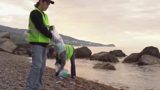 Covid-19 plastic afval. Gebruikte wegwerp medische maskers en handschoenen weggegooid door de golven. Vrijwilligers verzamelen afval aan de zeekust. Vervuiling van de oceaan tijdens een pandemische coronavirus — Stockvideo