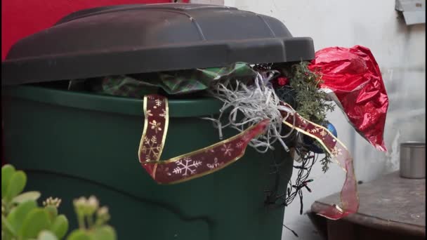 Kerstverspilling in een vuilnisbak. Milieuverontreiniging door kunststoffen. Gebruikt cadeaupapier, kerstboomverlichting, kerstversiering, vakantiekaarten, aluminiumfolie — Stockvideo