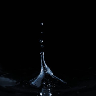 Düşen bir damladan, berrak su yüzeyine sıçrama ve dalgalanma. Karanlık bir arka planda