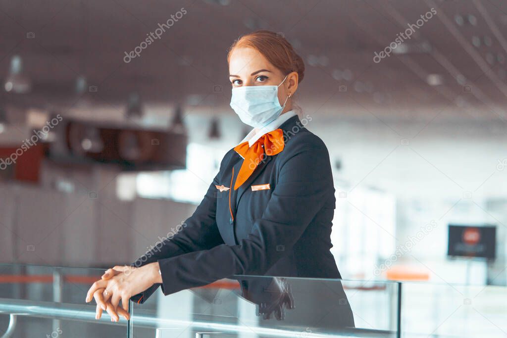 Close up Of Beautiful Red Head Flight Attendant Wearing Protecting Mask At Empty Airport. Airport Without Passengers and Light. Travelling During Epidema. Covid-19 Outbreak Travel Restrictions. Flight Cancellation.