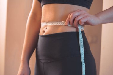 Vücut pozitiftir. Vücut Tarafsızlığı. Kendini sev. Kendini kabullenme. Spor Giyimli Genç Kadın Belini Ölçüyor