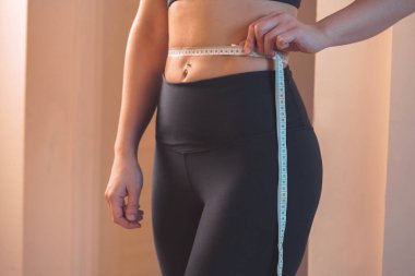 Vücut pozitiftir. Kendini kabullenme. Siyah spor kıyafetli genç bir kadın. Belini ölçüyor ve 60 cm 'den uzun olduğunu fark ediyor. Her türlü uyum ve ağırlıkta mutlu olmana izin ver.