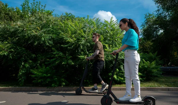 Young Couple Driving Electric Scooters City Park Sunny Summer Day ロイヤリティフリーのストック画像