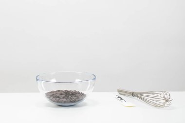 Yakın plan siyah çikolata, izole edilmiş beyaz arka planda cam kaseye çipler bırakıyor.