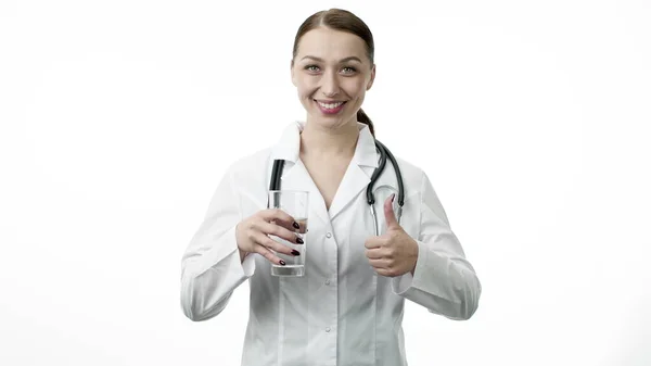 젊은 여성 의사가 깨끗 한 물 잔을 들고 엄지손가락을 위로 올려 놓은 간판처럼 보이는 모습 — 스톡 사진