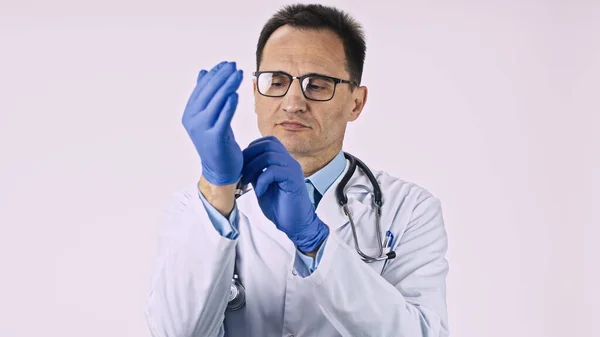 Erfahrener Proktologe mittleren Alters legt sterile medizinische Handschuhe in die Hände. — Stockfoto