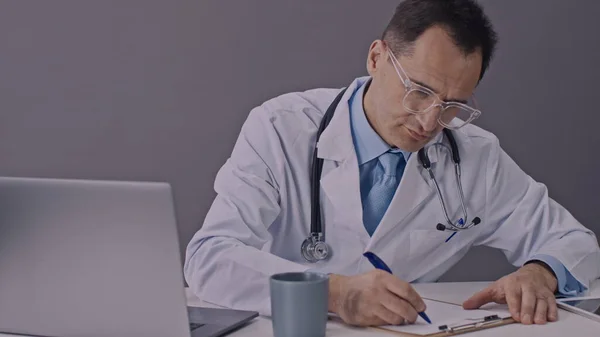 집중적 인 의사는 클립보드와 함께 책상 위에 누워 지친 의료 기록을 작성 한다 — 스톡 사진