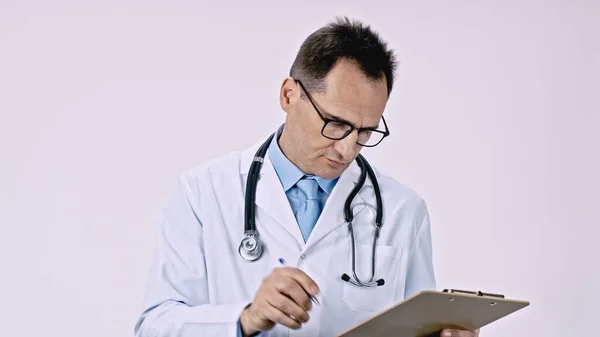 Seriöser Arzt holt Stift aus der Tasche und schreibt Rezept auf Klemmbrett — Stockfoto