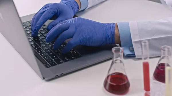 Χημικός σε γάντια σε εργαστήριο καινοτομίας δακτυλογράφησης σε φορητό υπολογιστή. Κοντινό πλάνο — Φωτογραφία Αρχείου