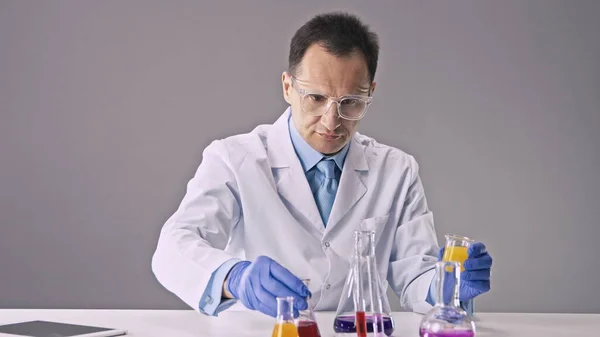 Laboratóriumi asszisztens fehér köpenyben keveri a többszínű vegyi anyagokat a kémcsövekben — Stock Fotó