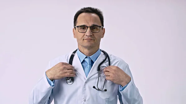 Hübscher Doktor im Laborkittel zieht Stethoskop an und untersucht Patienten auf weißem Hintergrund — Stockfoto