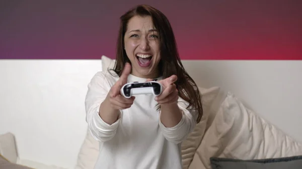 Joyeux attrayant femme en pyjama blanc joue à des jeux vidéo avec joystick au lit — Photo