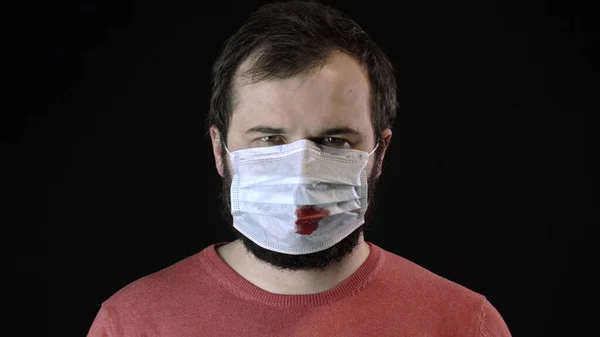 Больной человек в медицинской маске с кровью на ней надевает новую маску. Ковид-19 — стоковое фото
