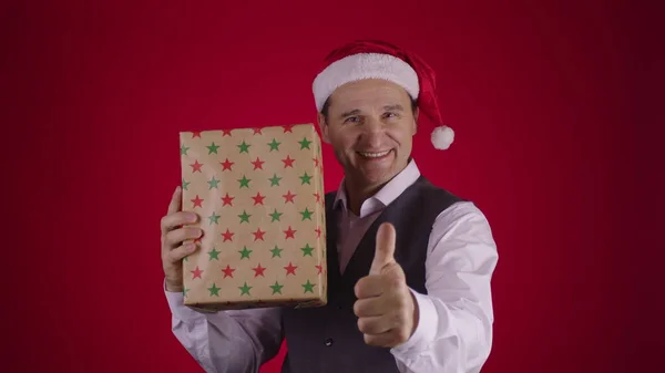 Šťastný vzrušený 40s muž v Santa klobouk chytání létání dárkové krabice a ukazuje palec nahoru — Stock fotografie
