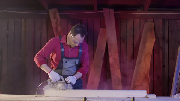 Carpenter cleans surface of wooden beam with electric planer and flies sawdust — Stock Photo, Image