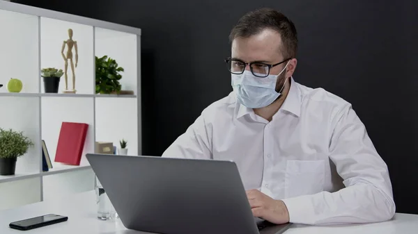Hombre de negocios guapo en máscara protectora trabajando remotamente en la computadora portátil en cuarentena — Foto de Stock