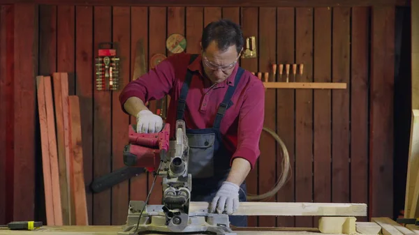 Man carpenter cuts a wooden beam with a circular saw in the workshop. — Stock Photo, Image