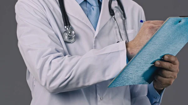 Docteur tient un dossier tablette dans les mains et écrit des données avec un stylo à bille — Photo