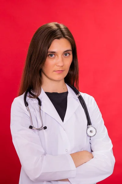 Atractiva morena de pelo largo doctora posando brazos cruzados en estudio rojo —  Fotos de Stock