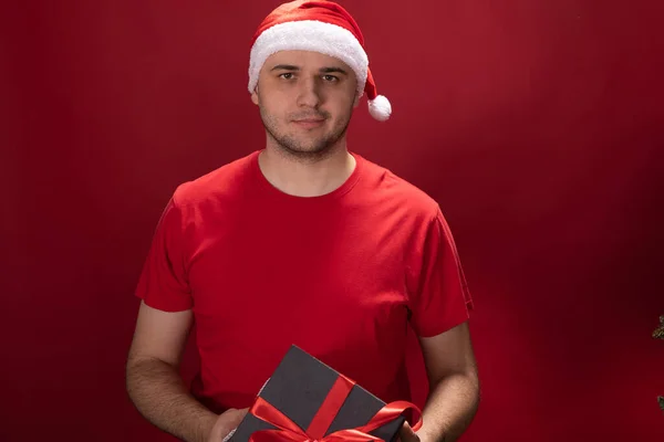Christmas gift delivery. Portrait of young man in santa hat holding xmas present — Stock Photo, Image