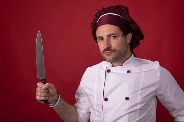 Chef masculino guapo sin afeitar que sostiene el cuchillo de los chefs que mira la cámara —  Fotos de Stock