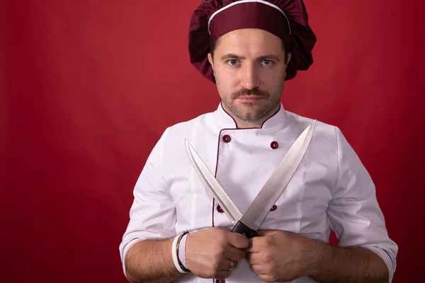 Cocinero o panadero hombre en chefs sombrero posando mirando cámara aislada sobre fondo rojo —  Fotos de Stock