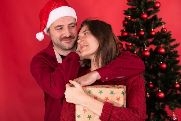 Felices abrazos de pareja delante del árbol de Navidad, diviértete sonriendo sobre fondo rojo — Foto de Stock