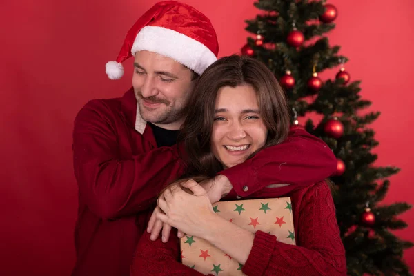 Couple joyeux câlins devant l'arbre de Noël, amusez-vous à rire sur fond rouge — Photo